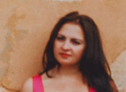 Woman with long dark hair wearing a pink top against a textured beige background.