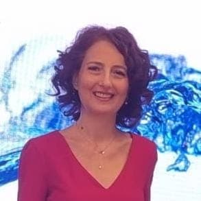 Smiling woman with curly dark hair wearing a red V-neck top and gold necklace.