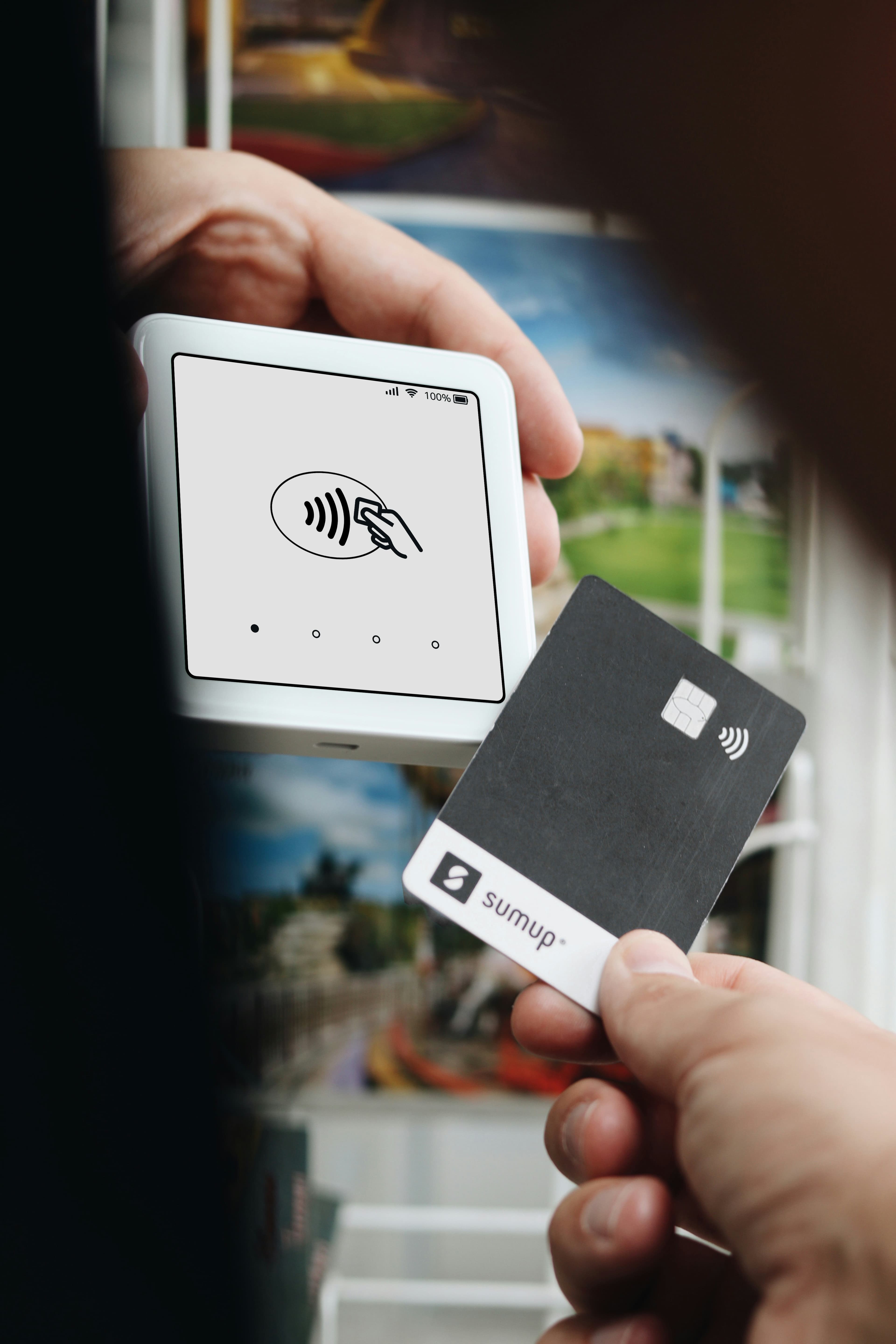 Hand holding a black SumUp card near a white contactless payment terminal for a transaction.